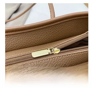 Detail of smooth gold zipper and pebble leather texture on a dark brown tote bag
