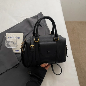 Sac Boston noir minimaliste avec détails dorés et bandoulière sur une veste grise