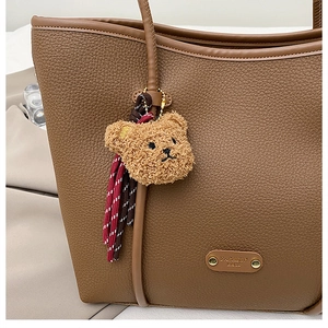 Detail of brown litchi grain leather tote bag with plush bear charm and gold emblem