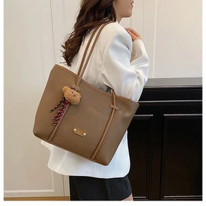 Detailed view of deep brown pebbled leather tote bag with a cute bear charm on a model