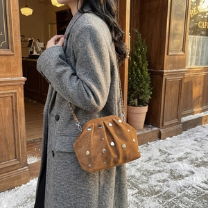 Brown rivet cloud bag with metal chain strap shown in a cozy outdoor winter setting
