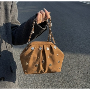 Close-up of brown suede bag with silver rivets and chain strap in natural outdoor sunlight