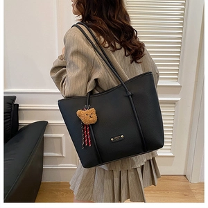 Side view of a large black textured leather tote bag with a cute brown bear charm
