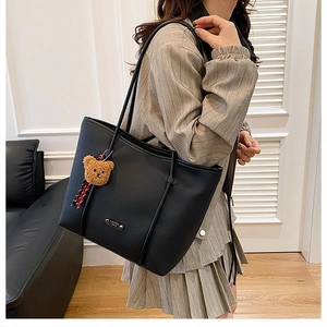 Detail of large black leather tote bag with brown plush bear charm and metal logo tag