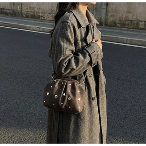 Detail of studded dark brown suede crossbody bag with gold rivets and metal chain strap
