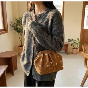 Detail of a brown suede cloud bag with silver studs and chain strap in a cozy room
