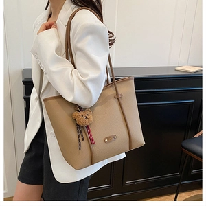 Detail of khaki leather tote bag with a cute bear pendant and metal logo detail