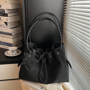 Minimalist black leather tote bag with star pendant and drawstring on white cabinet