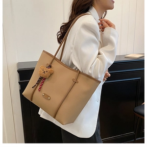 Detail view of khaki pebbled leather tote bag with metal logo and cute plush bear charm