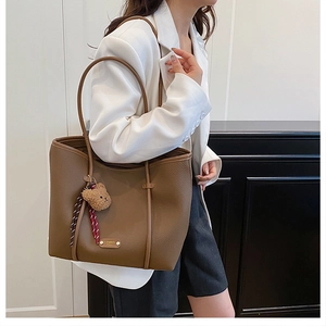 Detail view of brown pebbled tote bag with plush bear charm on white blazer outfit