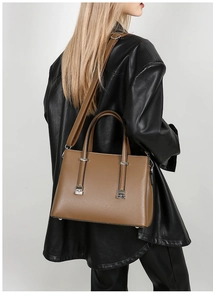 Detail of a brown leather tote bag with wide shoulder strap worn with a black coat