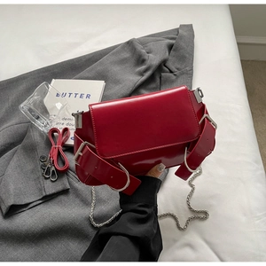 Detail of red glossy crossbody bag with adjustable buckles and chain strap on grey blazer