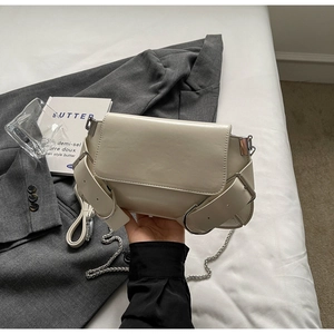 Detail of cream shoulder bag featuring silver chain strap and wide side buckle accent