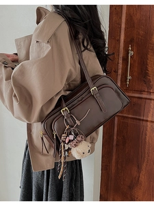 Detail of dark brown leather bowling bag with vintage buckle and plush bear charm