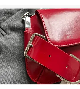 Close-up of red patent leather shoulder bag with silver textured metal buckle detail