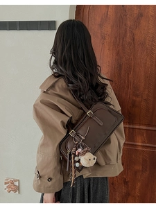 Detail of dark brown leather shoulder bag with bear pendant worn on person