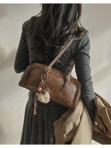 Close-up of vintage brown leather shoulder bag with cute white plush charm on a grey dress