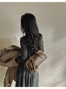 Brown leather shoulder bag with plush doll and star charms shown on model's back