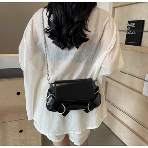 Model view of black glossy shoulder bag with metal chain strap and large buckle