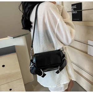 Detail of black glossy leather crossbody bag with silver buckles and large metal rings