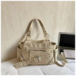 Detail of beige tote bag with decorative zippers and metallic eyelet belt on fabric
