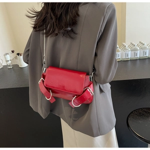 Detail of red glossy shoulder bag with metallic chain and buckle on female model