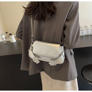 Detail of silver metallic crossbody bag with chain strap and buckle on modern blazer