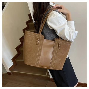 Vista detallada del bolso tote marrón con costuras blancas y detalles trenzados