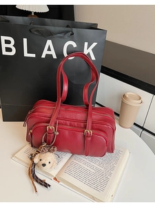 Detail of red faux leather shoulder bag with zipper pockets and a cute bear charm