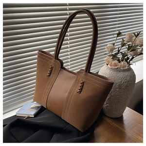 Detalle de bolso tote de cuero PU marrón con costuras blancas sobre mesa de madera