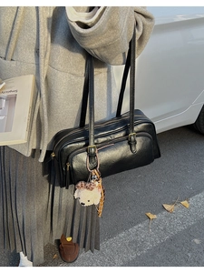 Detail of a black leather shoulder bag with double zippers and a plush puppy charm accessory