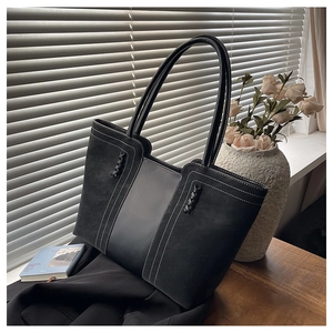 Detalle de bolso tote negro con costuras blancas en contraste y asa de hombro trenzada