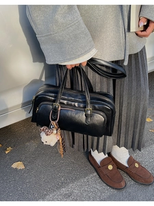 Detail of black leather Boston bag with dual zipper and a cute plush bear charm
