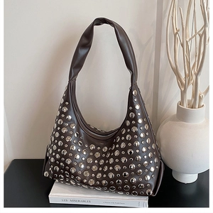 Detail of dark brown leather underarm bag with silver rivets on a minimalist book