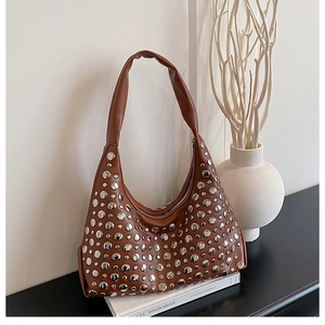 Close-up of brown shoulder bag with silver rivet studs on a white book display