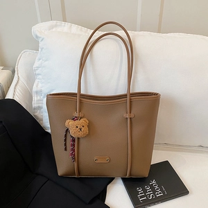 Classic brown tote bag with bear charm on a white sofa in a cozy interior setting