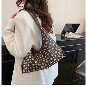 Close-up of a dark brown crescent hobo bag with silver metallic rivets on a white blazer