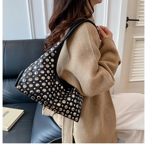 Detail of black hobo shoulder bag with silver rivet studs worn by a model in a cozy setting