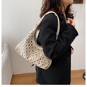 Detail of beige shoulder bag with silver rivet studs on black suit model outfit