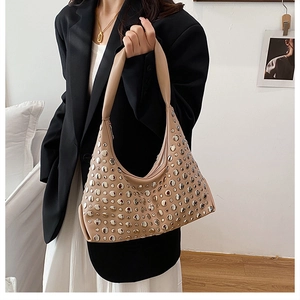 Beige leather hobo bag with silver metal rivets shown in a minimalist home setting