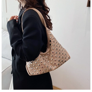 Beige moon-shaped hobo bag featuring silver rivets on a wide shoulder strap