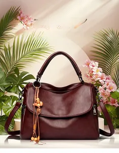 Détail d'un sac à main bordeaux en cuir grainé avec pompon en bois et décor floral
