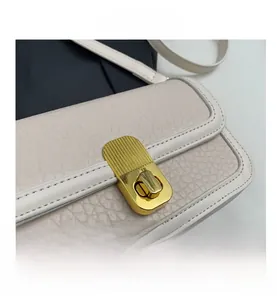 Close-up of cream square bag with wavy gold buckle and litchi grain texture