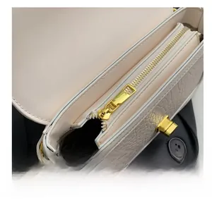 Close-up of smooth gold metal zipper and crocodile embossed texture on a cream crossbody bag