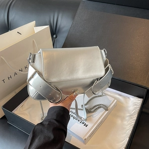 Silver metallic crossbody bag with chunky metal buckles and chain strap on a silk background