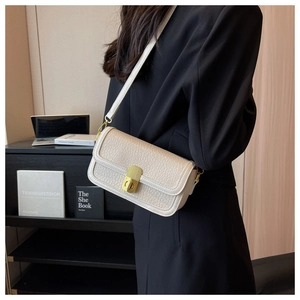 Detail of cream white leather crossbody bag with golden clasp worn by a model