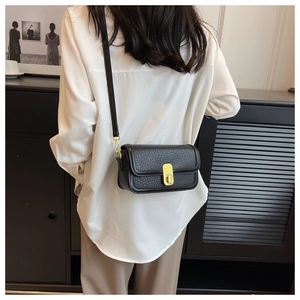 Detail of black pebbled crossbody bag with golden rectangular lock and slim shoulder strap