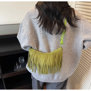 Green suede crossbody crescent bag featuring long decorative fringes and knotted strap design