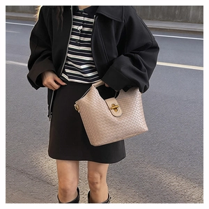 Close-up of beige woven leather handbag with gold twist lock and sturdy top handle