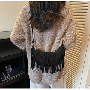 Detail shot of black suede crescent bag with long tassels and minimalist knotted shoulder strap